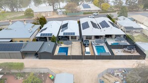Zona residencial con varias casas, cada una con paneles solares en los techos. Hay dos piscinas, una más grande y otra más pequeña, rodeadas de mobiliario exterior.
