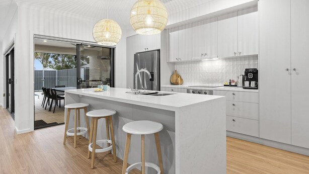 Una cocina moderna con una isla central, taburetes de bar, electrodomésticos de acero inoxidable e iluminación colgante.
