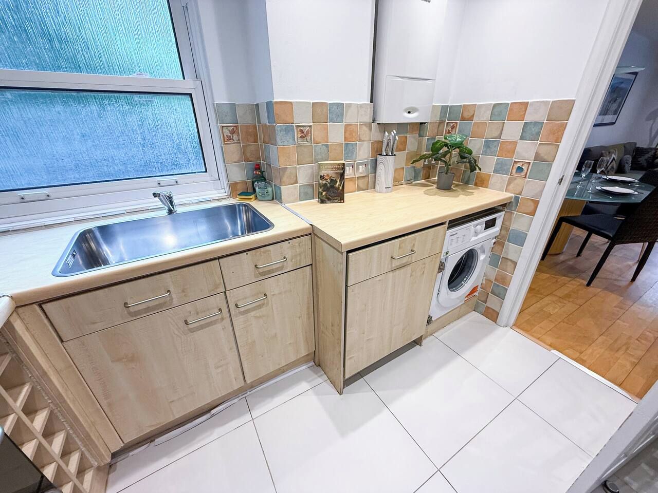 A compact kitchen with a sink, a washing machine, and a window.