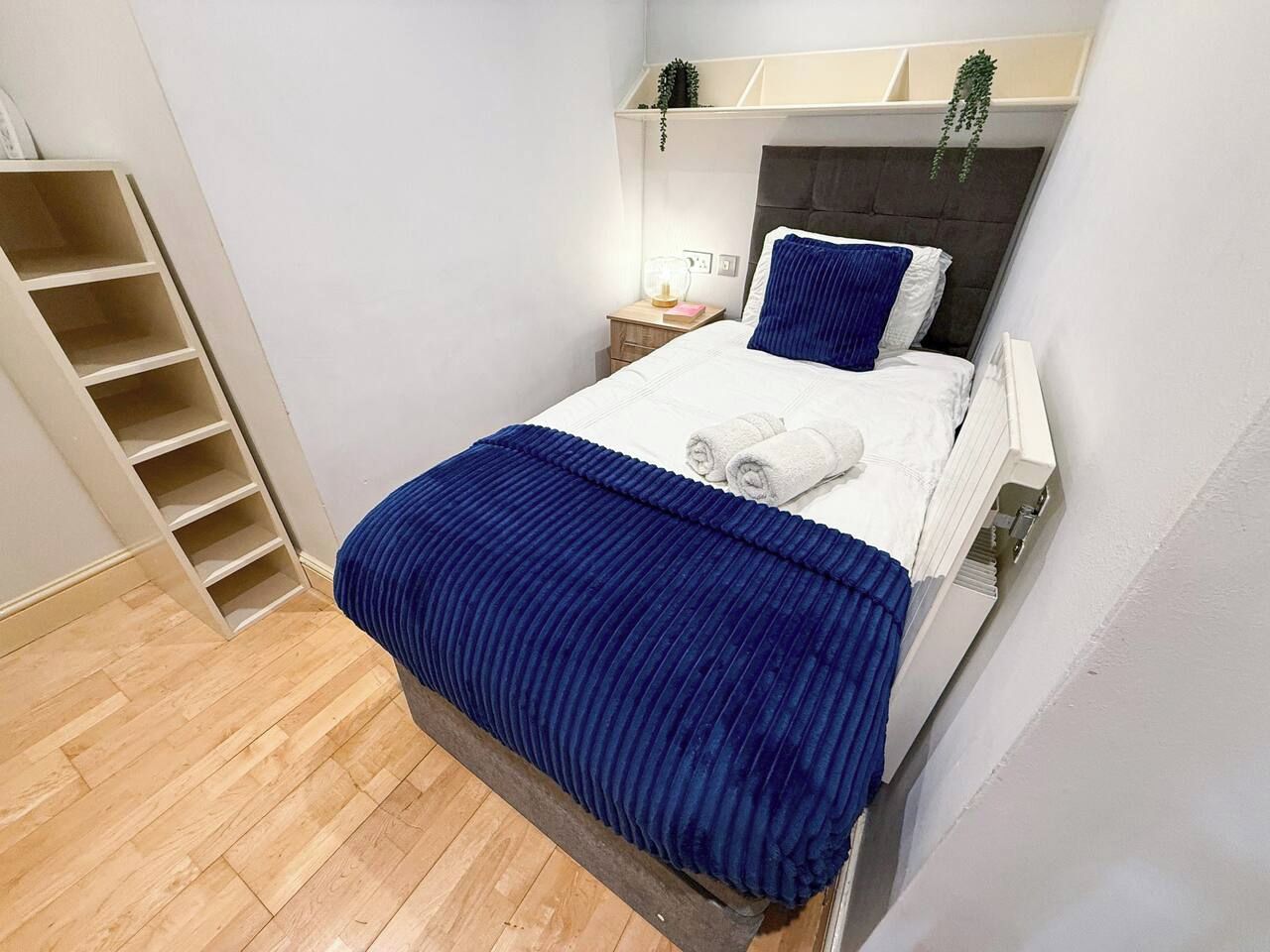 A bedroom with a bed, a nightstand, a shelf, and a wooden floor.