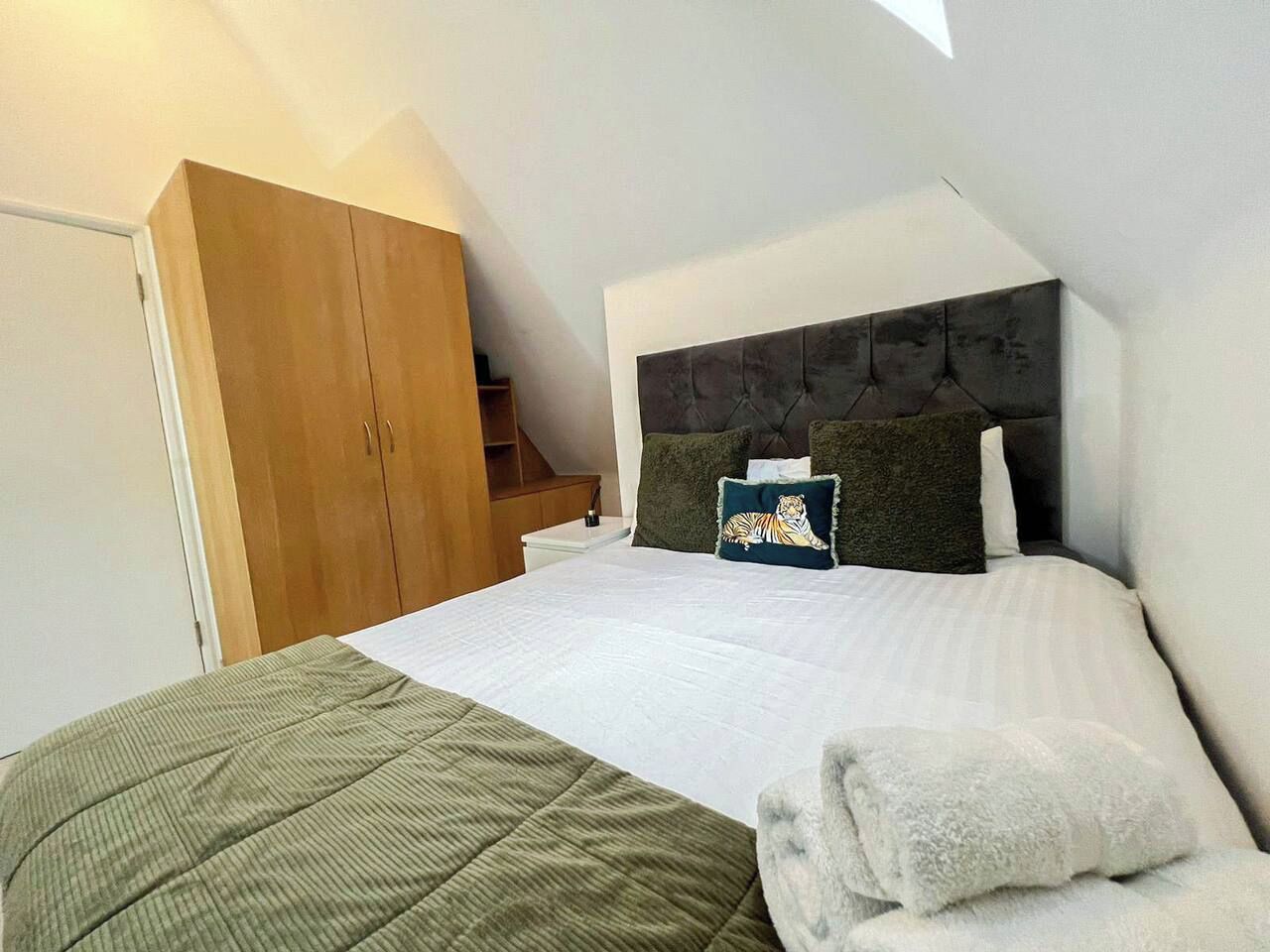 A bedroom with a bed, a headboard, a wooden wardrobe, and a staircase.