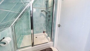 Una ducha con cerramiento de vidrio, una bañera blanca, un perchero y un ventanal.
