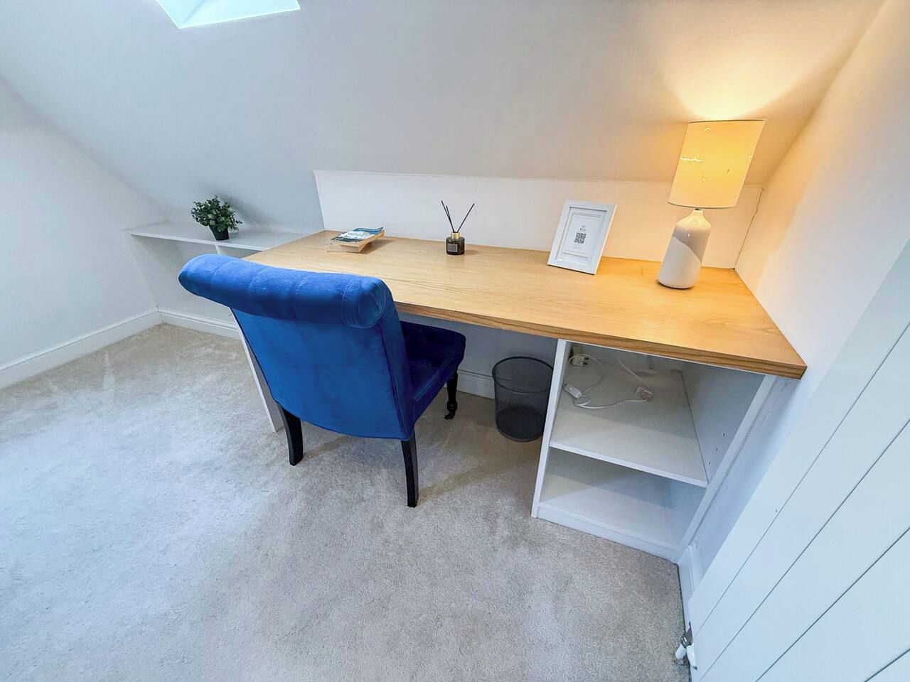 A small, well-lit room with a desk, chair, and shelving unit.