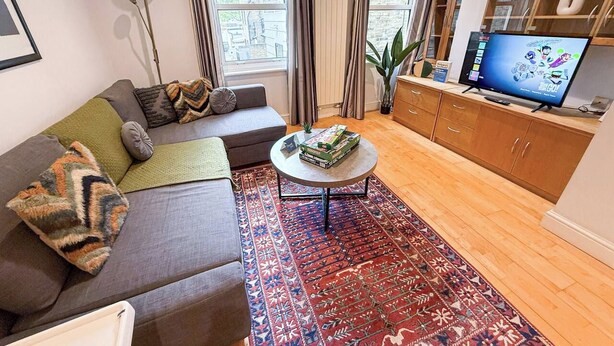 Una sala de estar con sofá, mesa de centro, televisor y una alfombra estampada.