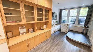 A room with a built-in wooden shelving unit, a washing machine, and a window with curtains.