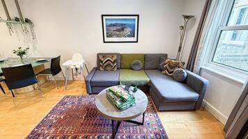 A living room with a sofa, a coffee table, a patterned rug, a dining area with chairs, and a framed picture on the wall.