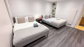 A modern bedroom with two beds, a bedside table with a lamp, and a built-in shelf unit.