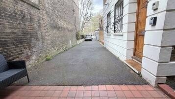 A narrow alleyway with a brick bench on the left, a white building with a wooden door on the right, and a car parked in the distance.