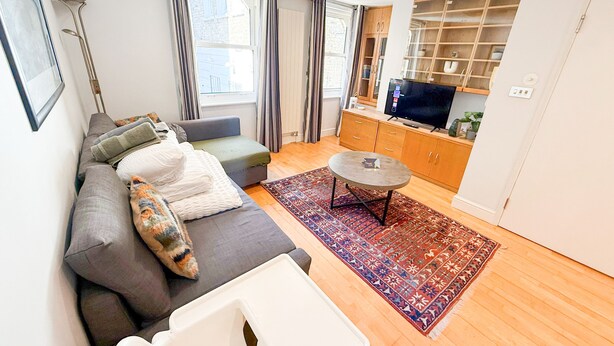 Una sala de estar moderna con un sofá gris, una mesita blanca pequeña y un televisor sobre un mueble de madera.