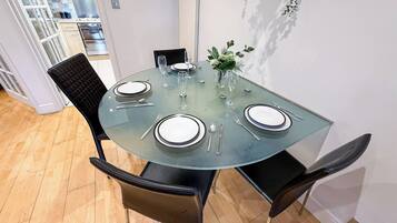 A round glass table with four chairs, a vase with greenery, and a kitchen in the background.