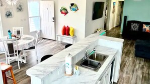 Una cocina moderna con encimera de mármol, un lavamanos y una zona de comedor con una mesa y sillas blancas.