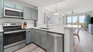 A modern kitchen with stainless steel appliances, grey cabinets, and a large window offering a view of the outdoors.