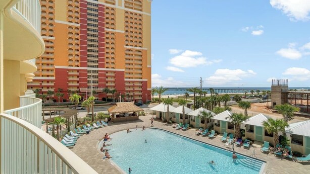 A hotel with a large pool, a beach view, and a high-rise building in the background.