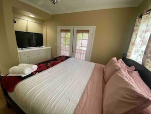 Un dormitorio con cama, televisor, armario y ventana con cortinas.