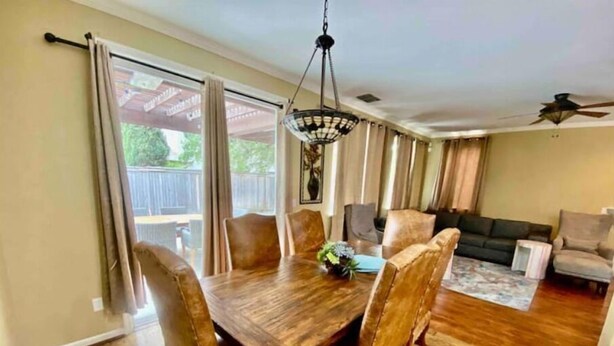 Un comedor con una mesa y sillas de madera, un candelabro y vistas al jardín trasero a través de amplios ventanales.