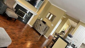 Una sala de estar con chimenea, un televisor de pantalla plana montado encima y un comedor con mesa y sillas.