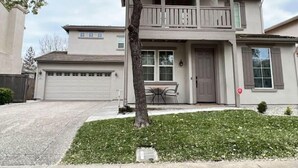 Una casa de dos pisos con balcón, garaje y un pequeño jardín delantero con un árbol.