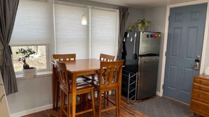 A compact kitchen with a dining table, chairs, a refrigerator, and a blue door. - The Fox Den (Ames)