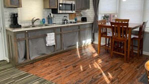A kitchen with a wooden island, a microwave, and a dining area with chairs. - The Fox Den (Ames)