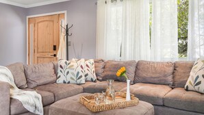 A living room with a sectional sofa, a tray with glasses and a vase, and a door with a coat rack.