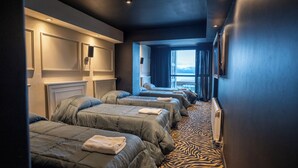 A hotel room with three beds aligned in a row, a zebra-patterned carpet, and a large window offering a view of the mountains. - Hotel Vuriloche Suites (San Carlos de Bariloche)