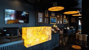 A modern bar area with a marble reception desk, a flat-screen TV, and framed pictures on the wall. - Hotel Vuriloche Suites (San Carlos de Bariloche)