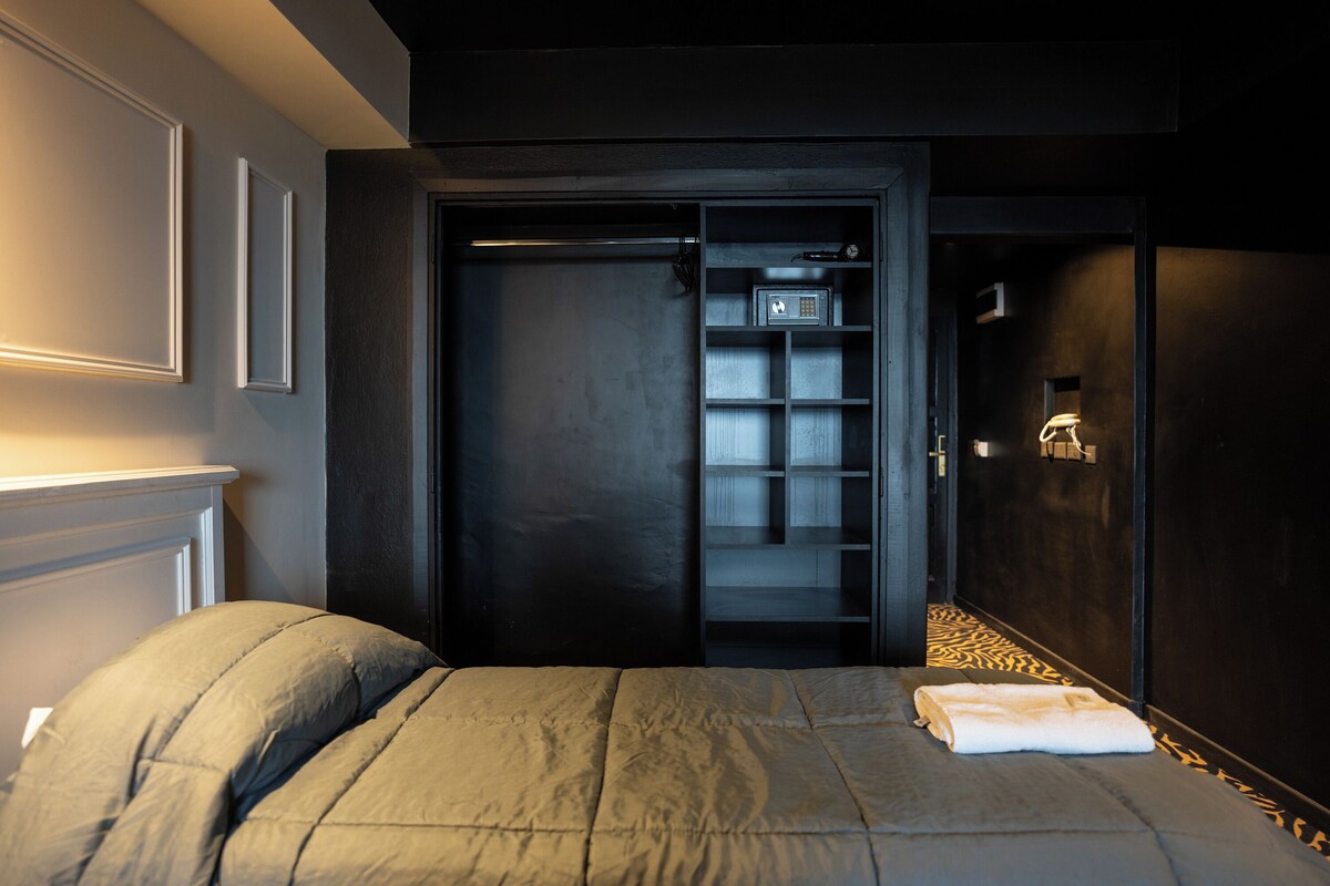 A hotel room with a bed, a wardrobe, and a door leading to a bathroom.