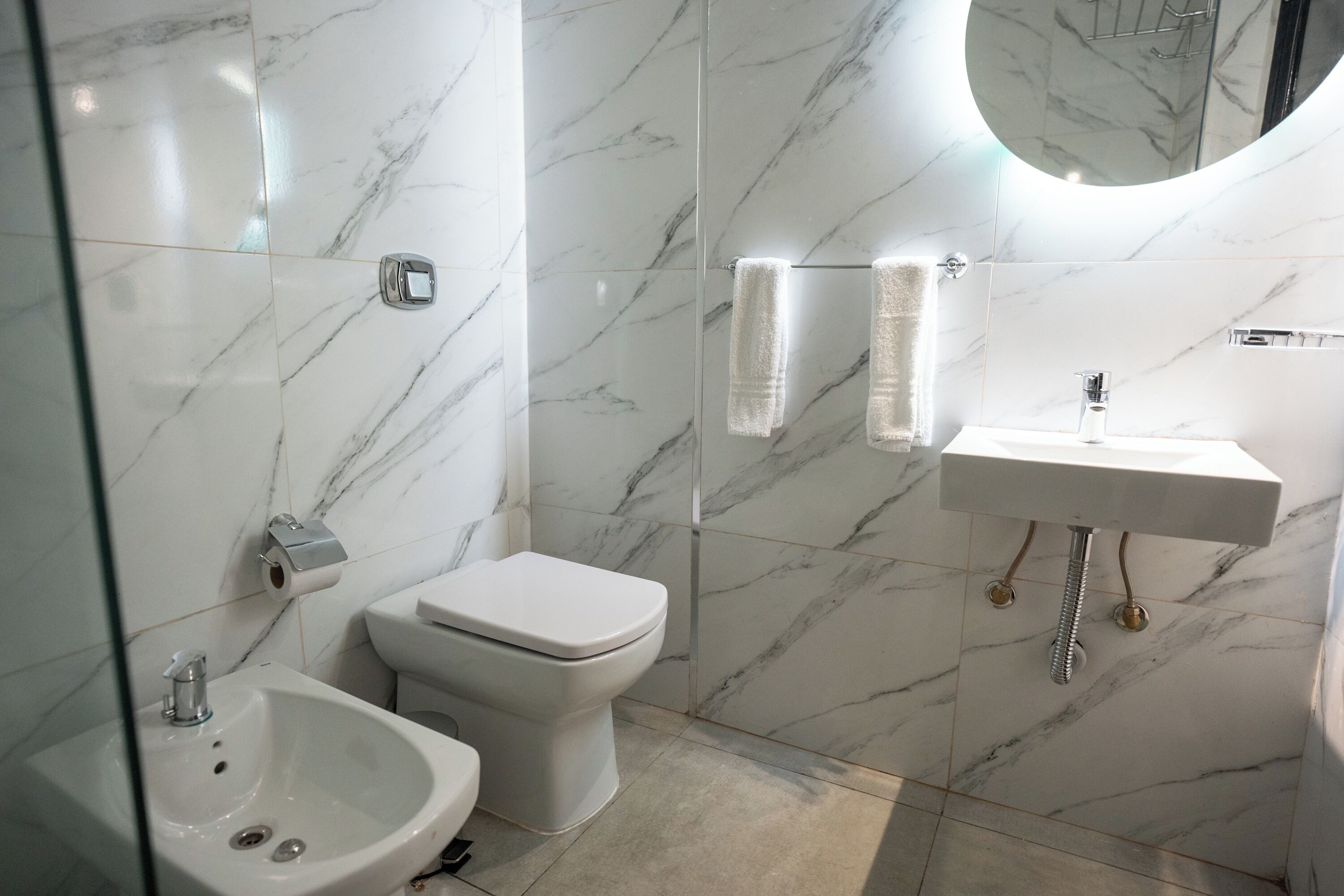 Un baño con piso de mármol, un lavamanos, un inodoro y un bidé.