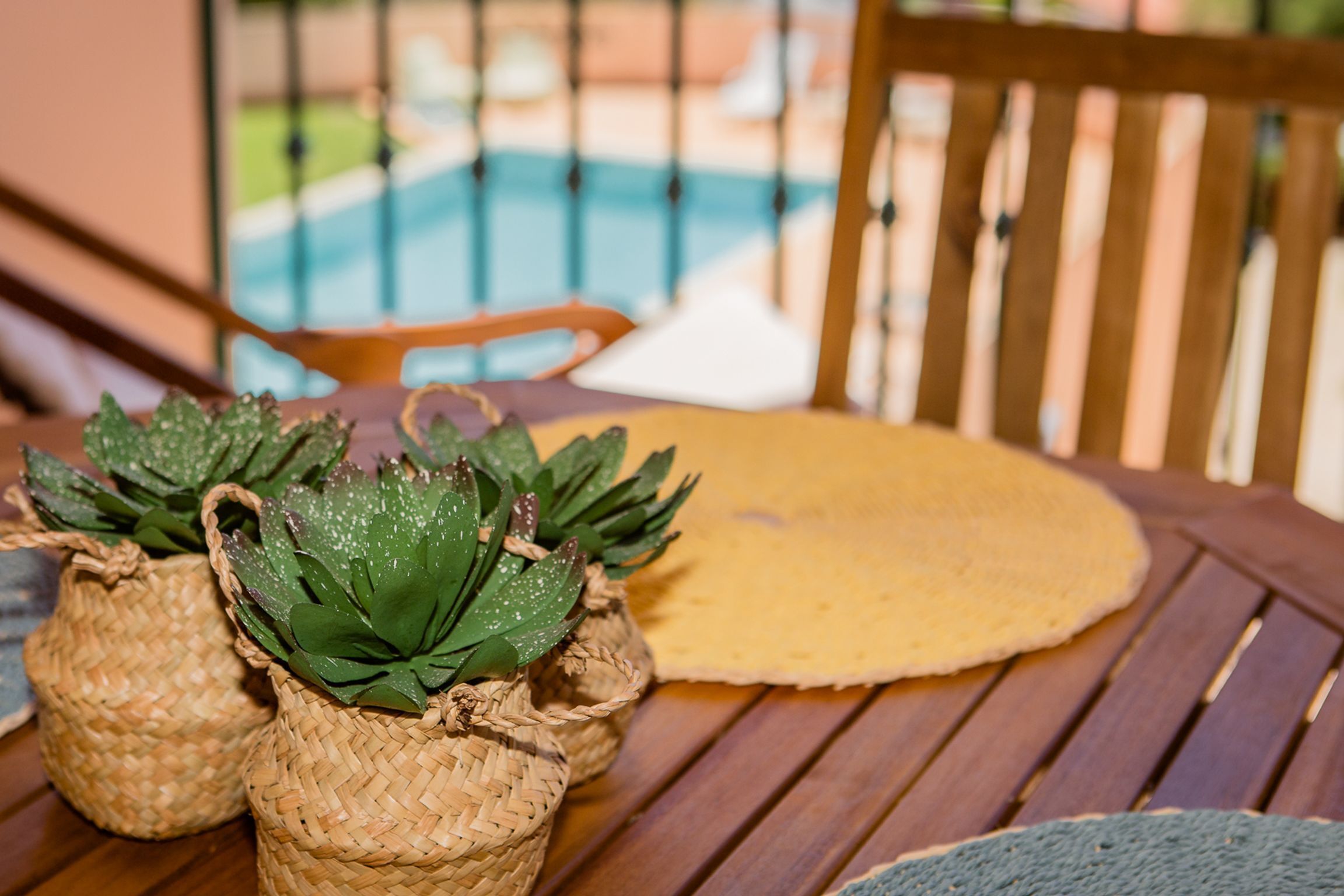 A wooden table with woven baskets containing green plants, a yellow placemat, and a wooden chair.