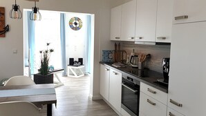 Una cocina moderna con armarios blancos, electrodomésticos de acero inoxidable y una zona de comedor con mesa y sillas de madera.