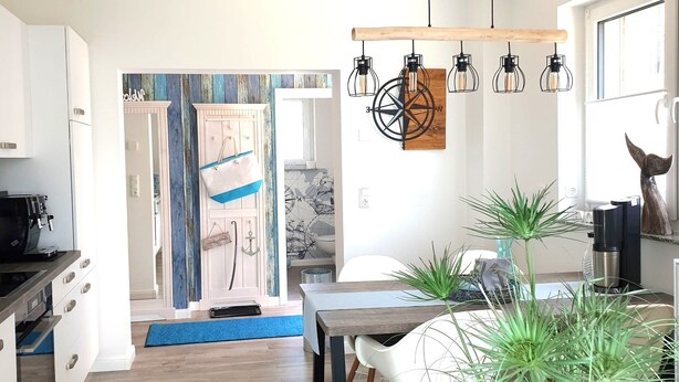 Una cocina moderna con armarios blancos, una cafetera y un comedor con mesa y sillas.