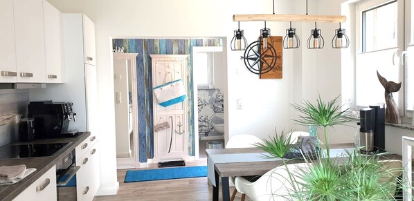 A modern kitchen with white cabinets, a coffee machine, and a dining area with a table and chairs.