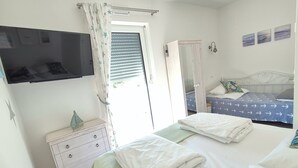 Un dormitorio con cama, cómoda, armario, televisor y ventana con cortinas.