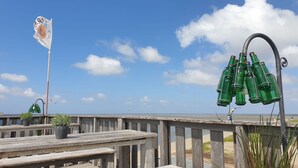 Una terraza de madera con bancos y plantas en macetas, con vista a una playa y un cielo despejado.
