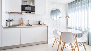 A modern kitchen with white cabinetry, a Bosch oven, and a dining area with white chairs and a round table. - VIVA  Marquês Studio (Porto)