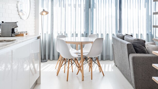 A modern kitchen with white cabinets, a dining area with a white table and chairs, and a grey sofa. - VIVA  Marquês Studio (Porto)