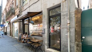 A street-side café with outdoor seating, a chalkboard menu, and a visible storefront. - VIVA  Marquês Studio (Porto)