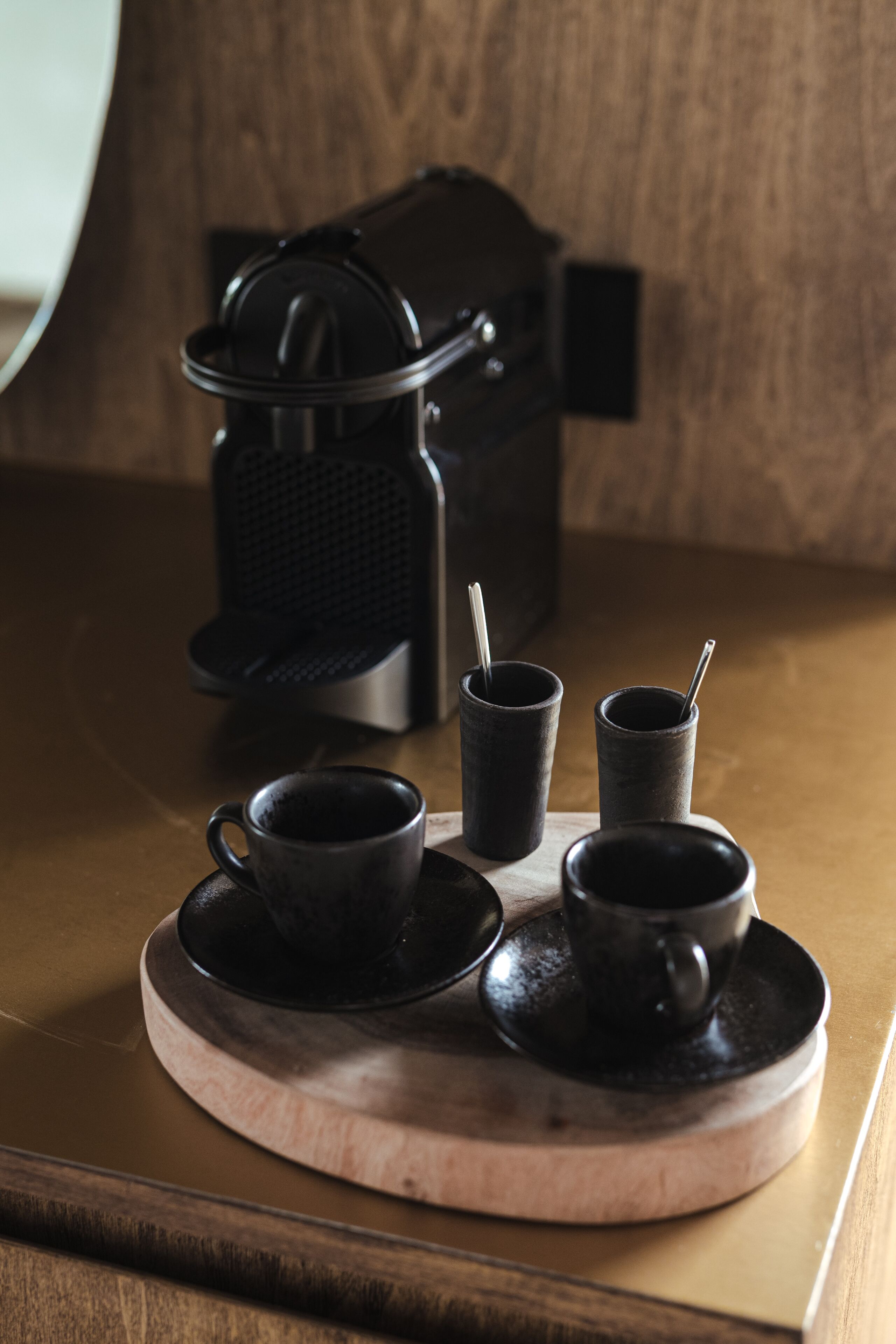 A coffee maker, two cups, and a saucer on a wooden tray.