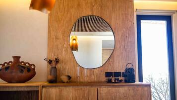 A wooden vanity with a round mirror, a vase, and a small table with a cup and a bag.