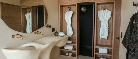 A modern bathroom with a large bathtub, wooden vanity, and two wooden robes hanging on hooks.