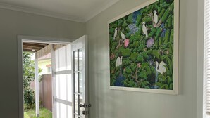 Um corredor com um banco branco, uma porta que dá para o exterior e um quadro de pássaros e flores na parede.