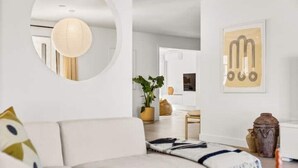 Ein modernes Wohnzimmer mit einem weißen Sofa, einem runden Spiegel, einer Pendelleuchte und einem gerahmten abstrakten Kunstwerk an der Wand.