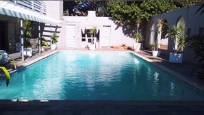 Une piscine bordée de pierres, entourée de plantes en pot et dotée d’un espace couvert avec un toit.