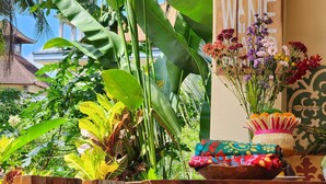 A tropical setting with lush green foliage, a wooden sign that reads "A MEAL WITHOUT WINE", and a table with a colorful bowl and a vase of flowers. - Danaya's villa (Ubud)