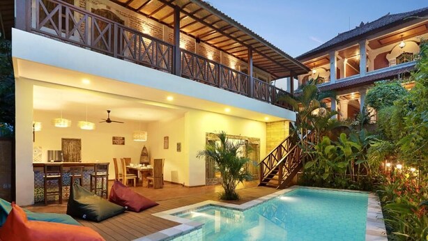 A modern poolside area with a wooden deck, seating, and a staircase leading to an upper level. - Danaya's villa (Ubud)