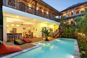 A modern poolside area with a wooden deck, seating, and a staircase leading to an upper level. - Danaya's villa (Ubud)