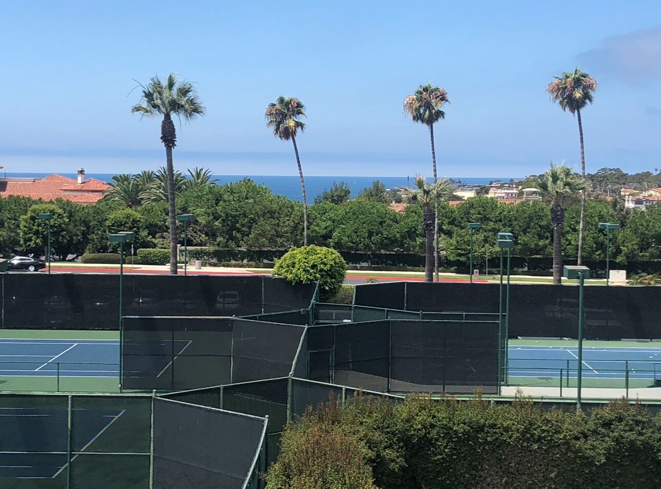 Una cancha de tenis con zonas verdes y vista al océano.