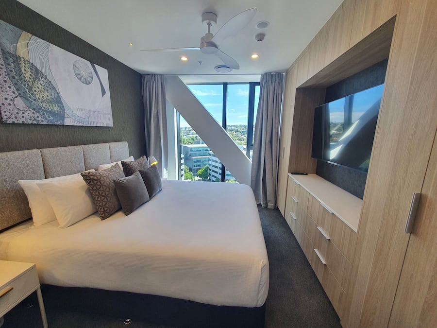 A modern hotel room with a large bed, a TV, and a view of the city.