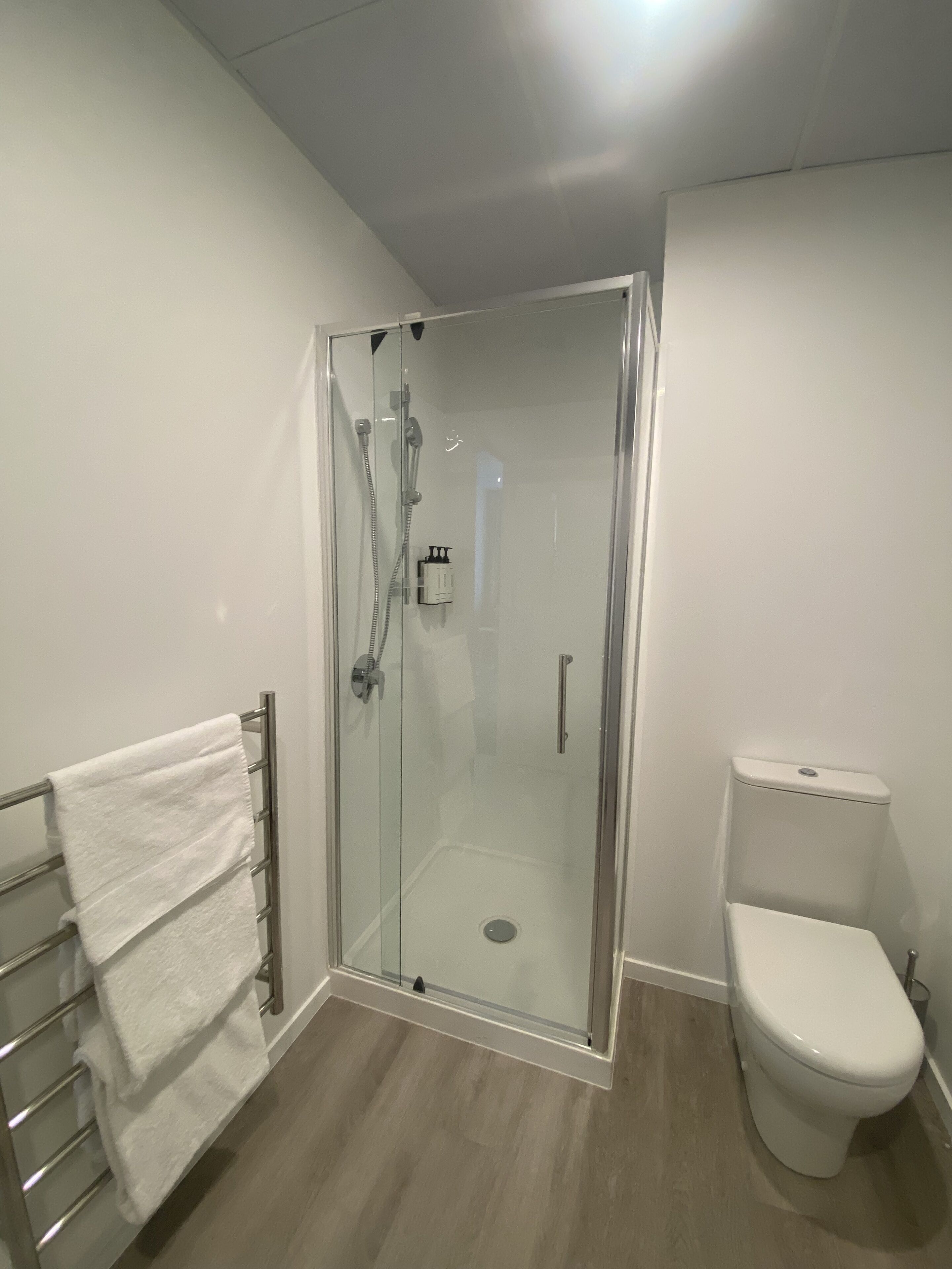 Un bagno moderno con doccia vetrata, un water bianco e un portaserviti con asciugamani bianchi.