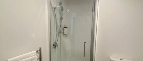 A modern bathroom with a glass-enclosed shower, a white toilet, and a towel rack with white towels.